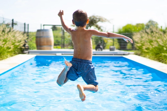 Ein Kind springt von hinten in einen Swimmingpool.